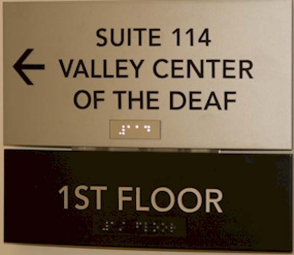 A picture of the sign for the entrance to Valley Center of the Deaf is shown. A braille is on the sign and beneath the sign it reads First Floor.
